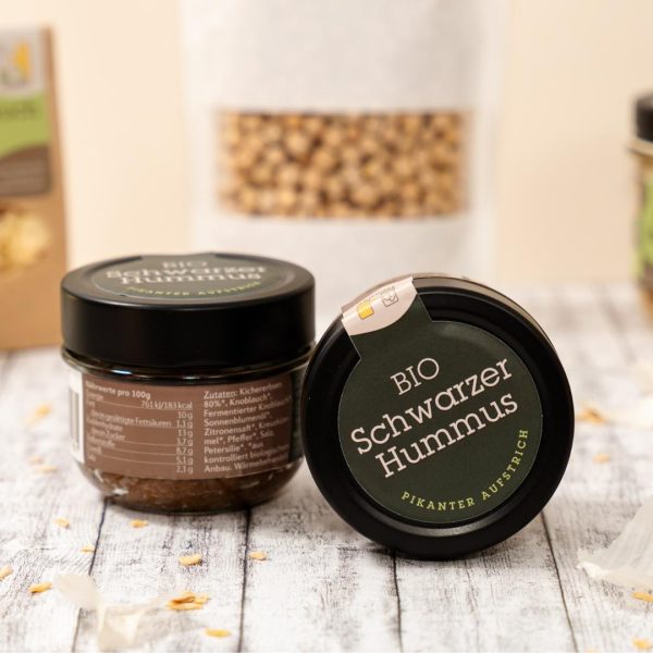 Schwarzer Hummus im Glas im Vordergrund, im Hintergrund weitere Bio-Produkte vom Hof Herbst.
